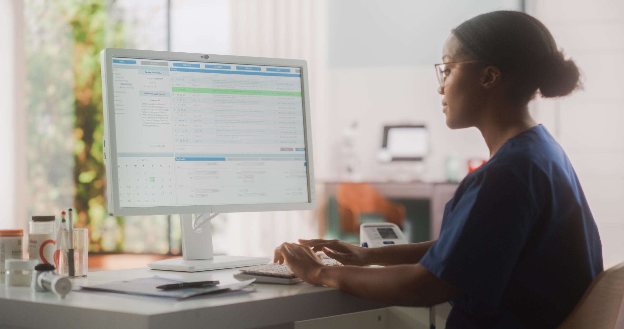 Healthcare professional typing on a computer, displaying patient data, with medical supplies visible on the desk.